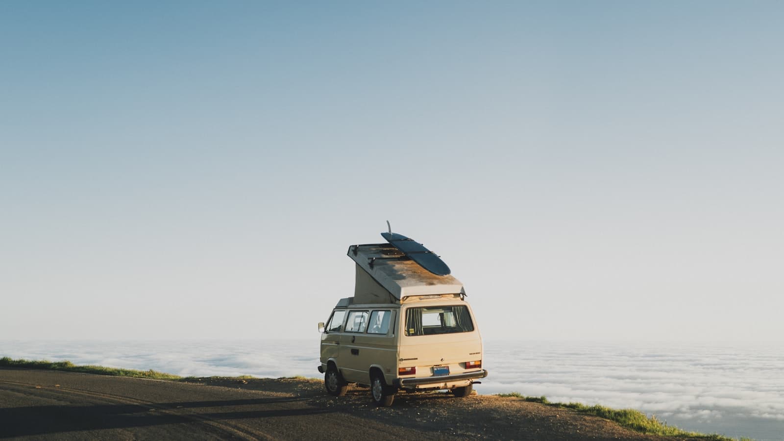 Van pop-top avec planche de surf au-dessus d’une mer de nuages à la lumière dorée