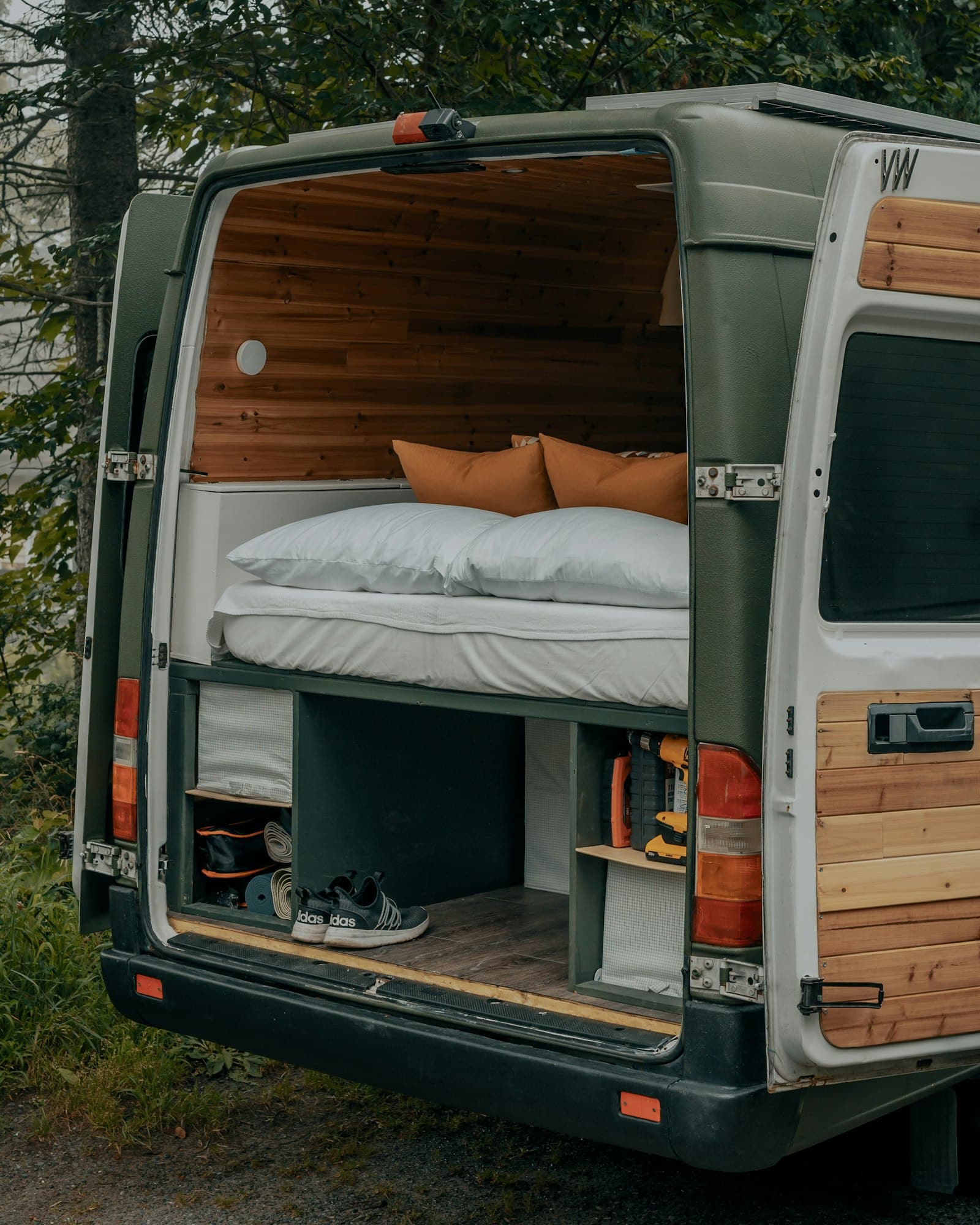 Intérieur d'un van aménagé, couchage et boiseries, portes arrière ouvertes en forêt