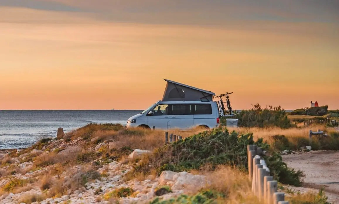Van aménagé VW California Ocean toit relevé, garé face à l'océan au coucher du soleil près de Bordeaux