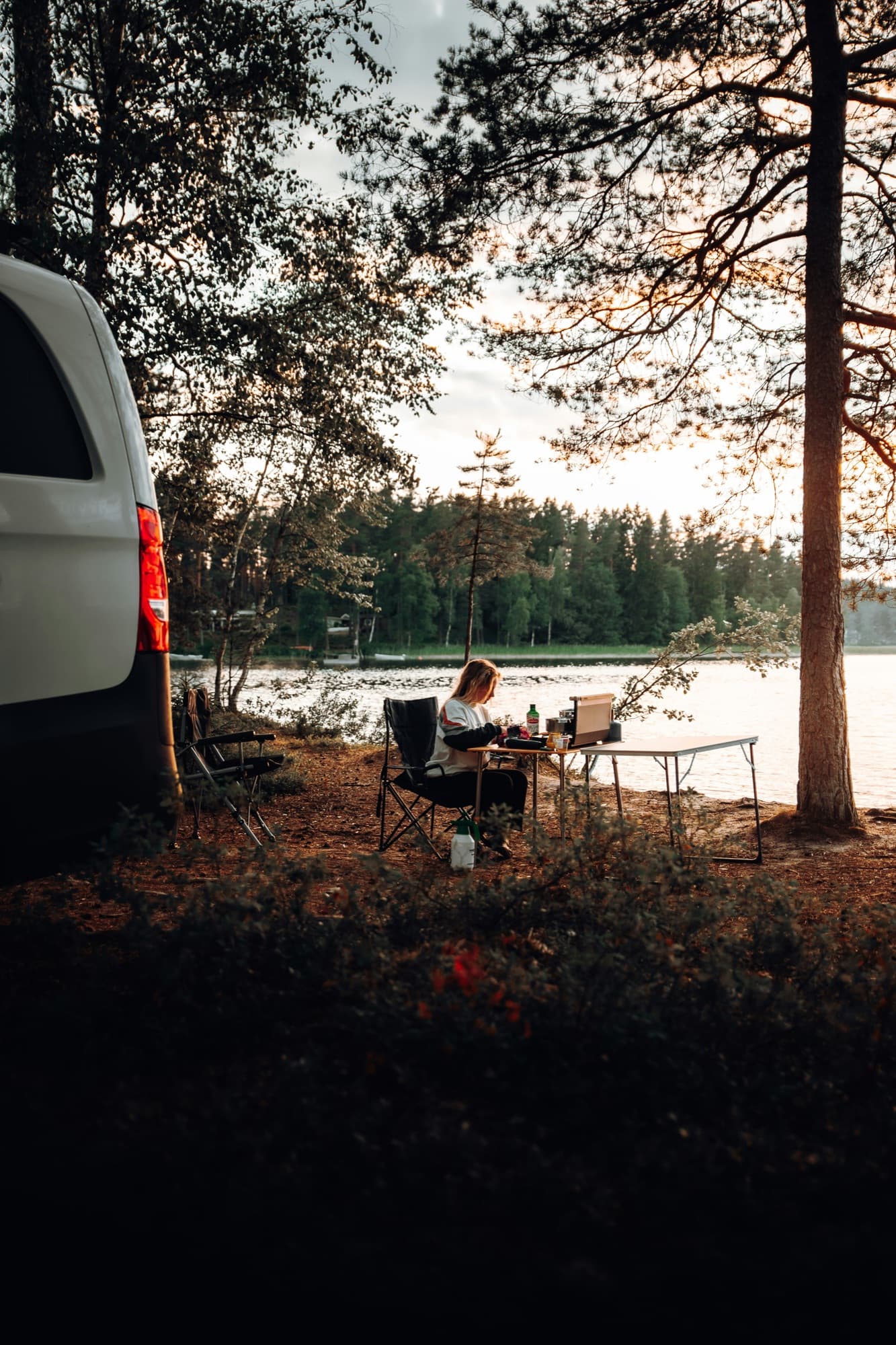 Voyageuse préparant son repas au bord d'un lac au coucher du soleil, à côté de son van